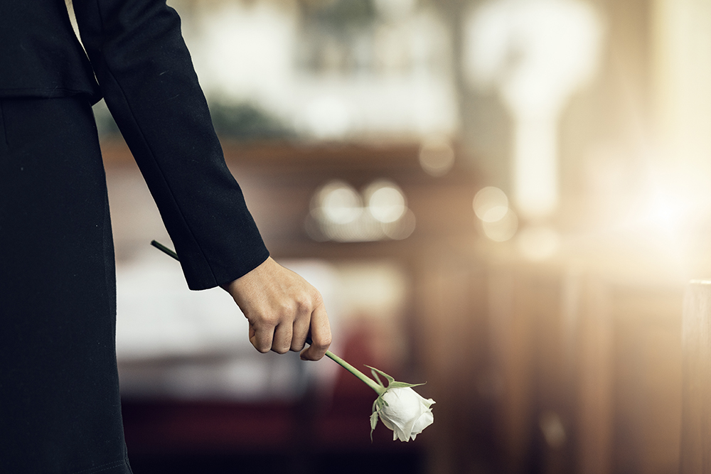 nabestaande houdt een witte roos in de hand tijdens een begrafenis